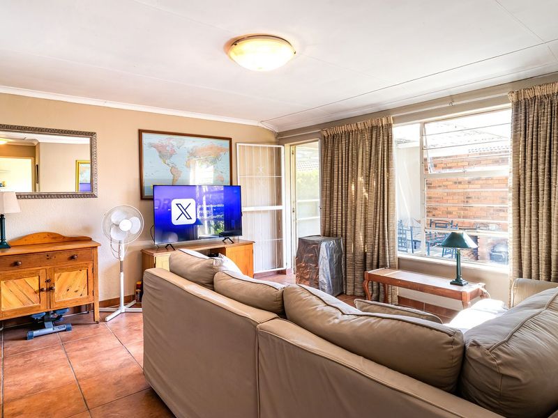 A comfortable living room featuring tiled flooring, a large window providing natural light, and direct access to an outdoor area through a security gate.