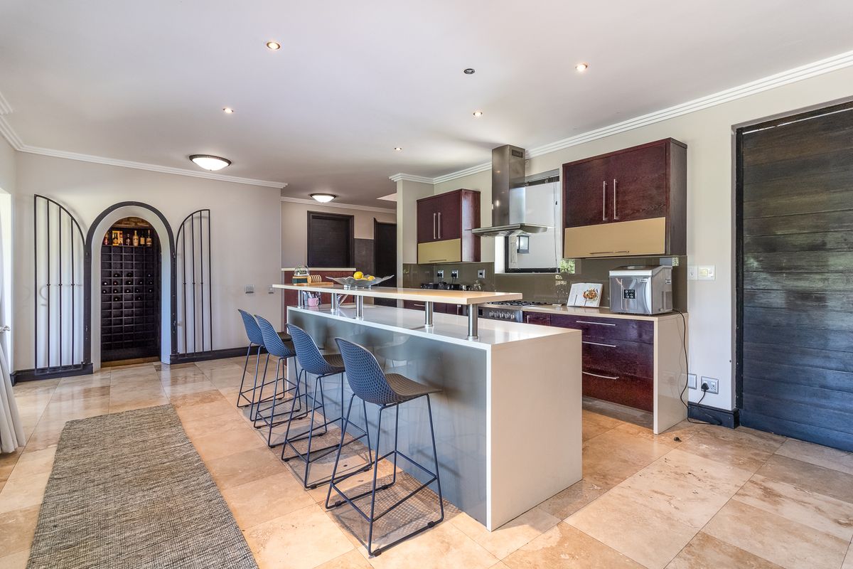 Modern open-plan kitchen featuring a large island with stone countertops, dark wood cabinetry, integrated appliances, and an adjacent arched wine cellar entrance.