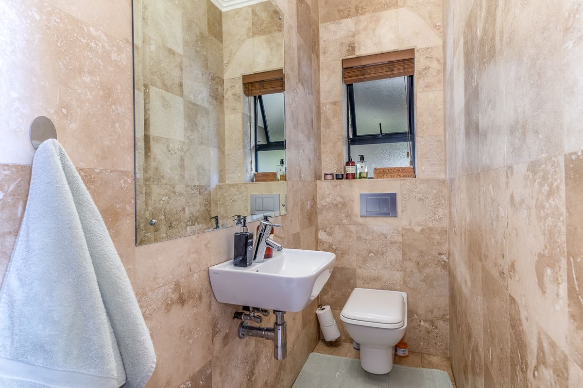 A compact, modern guest bathroom featuring floor-to-ceiling travertine tiling, a wall-mounted basin, and a concealed cistern toilet.