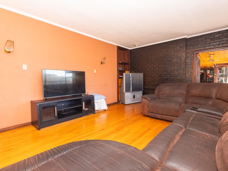 Living room featuring hardwood flooring, an exposed brick feature wall, and built-in shelving, offering a functional space with potential for modern updates.