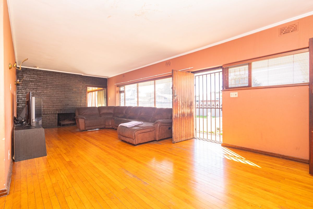 Spacious living room featuring hardwood flooring, a prominent brick fireplace, and direct access to the exterior through a security gate and timber door.