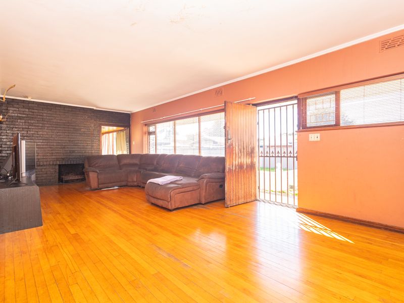 Spacious living room featuring hardwood flooring, a prominent brick fireplace, and direct access to the exterior through a security gate and timber door.