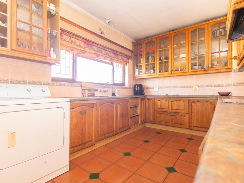 A dated kitchen featuring wooden cabinetry, tiled flooring, and a tiled backsplash, with visible ceiling damage requiring repair.