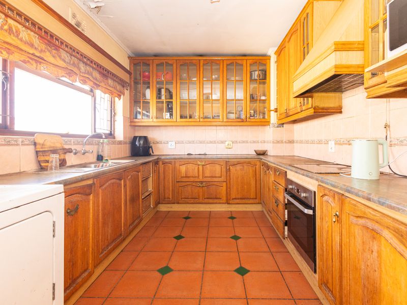A dated kitchen featuring traditional wooden cabinetry, terracotta flooring, and a tiled backsplash, offering significant potential for a modern renovation.