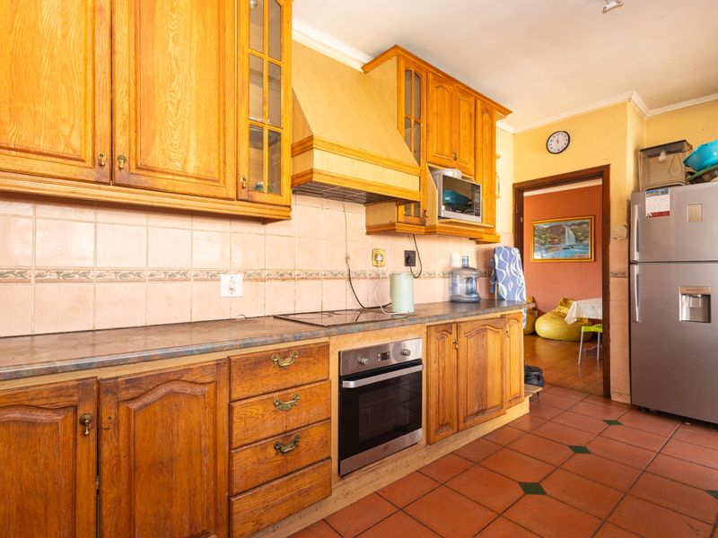 A functional kitchen featuring traditional wooden cabinetry, built-in oven, electric hob, and terracotta floor tiles, offering a classic layout with ample storage space.