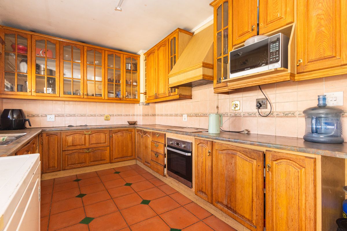 A traditional kitchen featuring extensive wooden cabinetry, built-in oven, extractor fan, and terracotta floor tiles with a tiled backsplash.