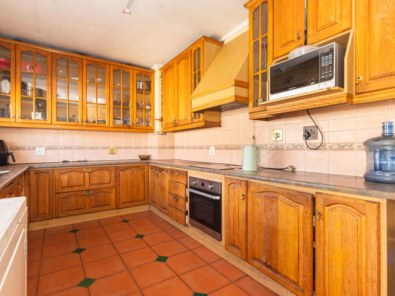 A traditional kitchen featuring extensive wooden cabinetry, built-in oven, extractor fan, and terracotta floor tiles with a tiled backsplash.