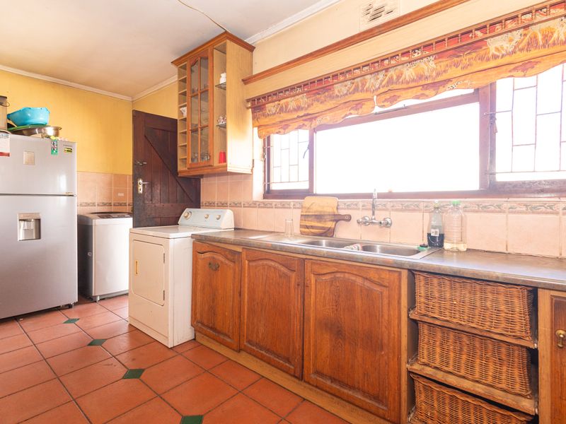A dated kitchen featuring wooden cabinetry, terracotta floor tiles, and a double basin sink with a tiled splashback.
