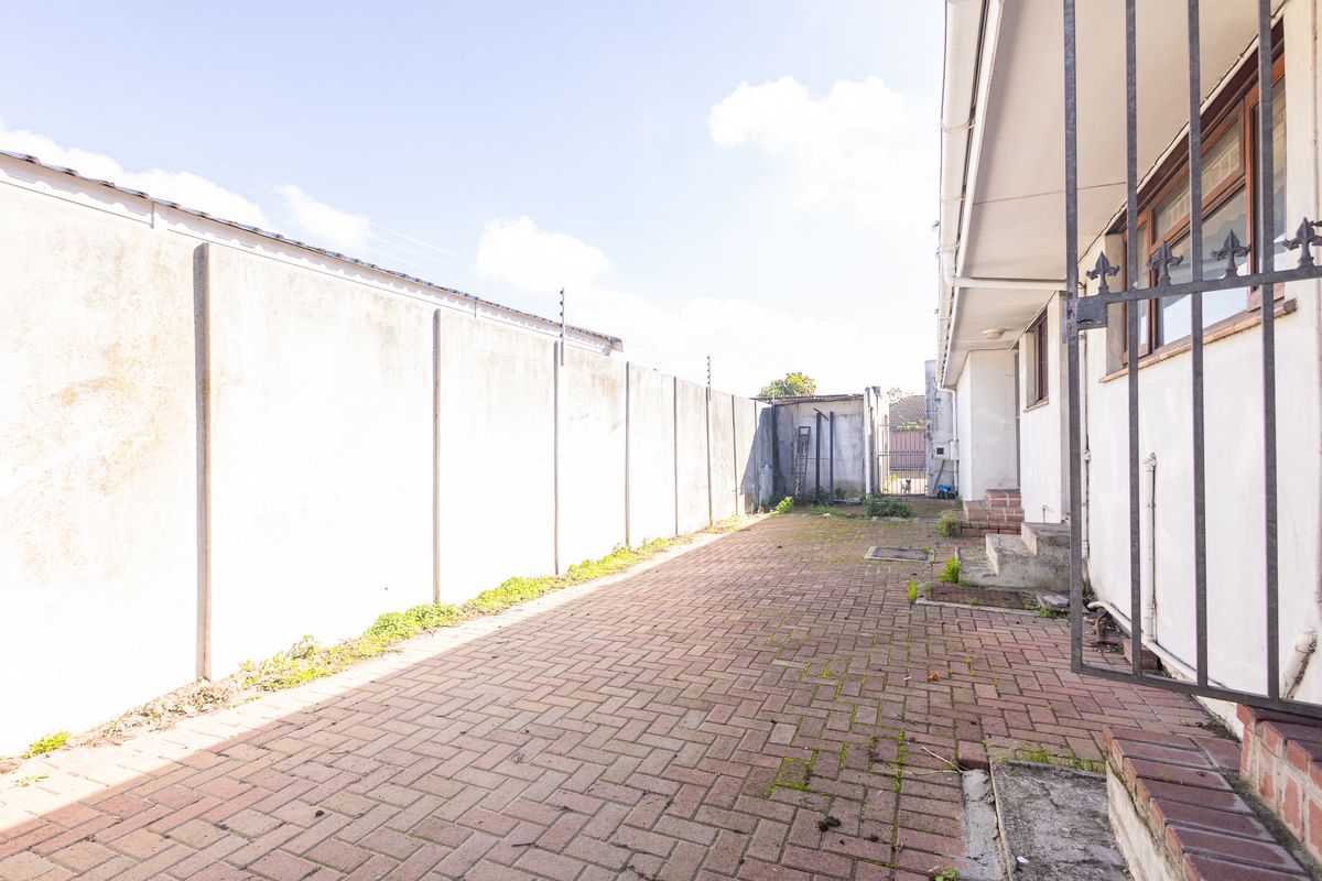 A side exterior area featuring a brick paved pathway, high precast concrete boundary walls with electric fencing, and a security gate.
