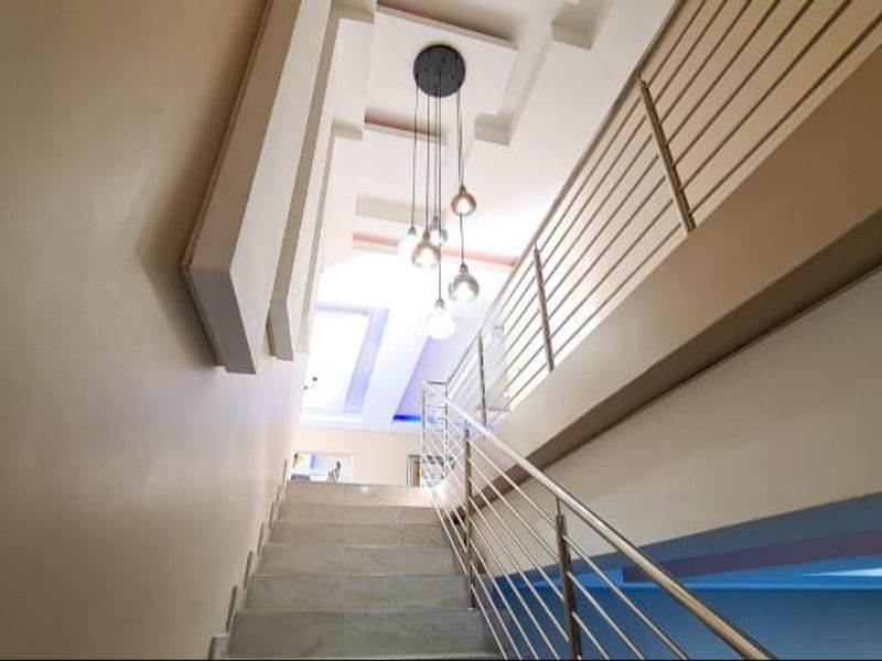 A bright, modern staircase featuring a stainless steel balustrade, recessed ceiling architectural details, and a contemporary multi-pendant light fixture.