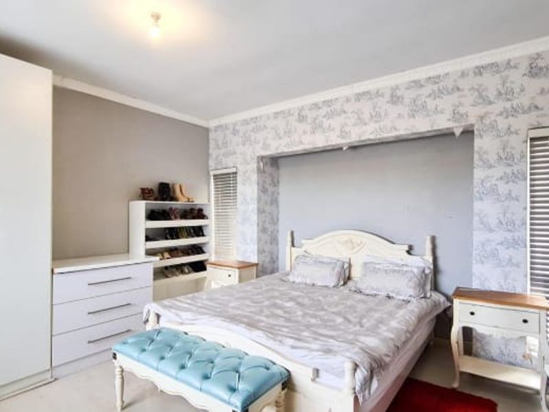 A bedroom featuring a built-in wardrobe, patterned wallpaper accent wall, and venetian blinds on the windows.