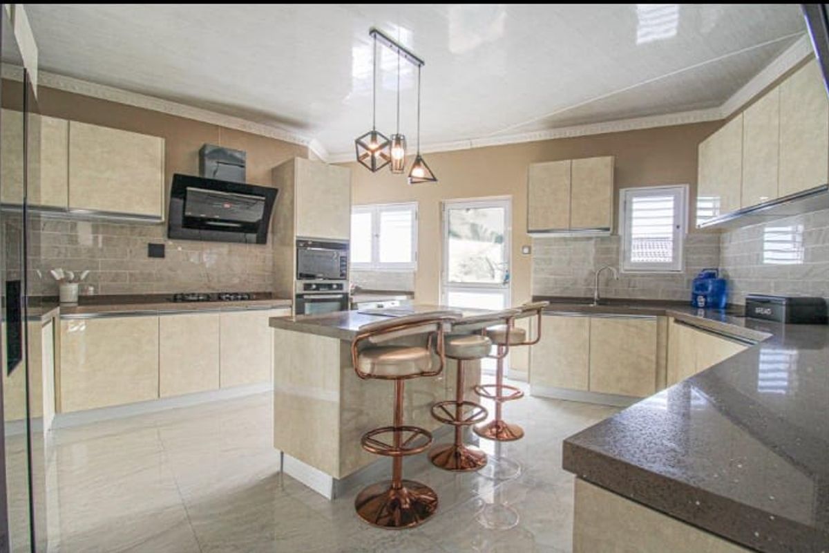 Modern kitchen featuring high-gloss cabinetry, stone countertops, a central island with breakfast bar seating, and integrated appliances.