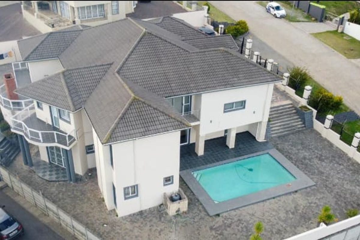 Aerial view of a multi-level residential property featuring a tiled roof, swimming pool, paved outdoor areas, and perimeter boundary walls.