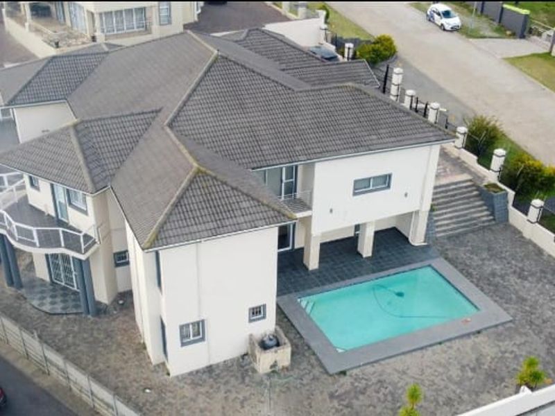 Aerial view of a multi-level residential property featuring a tiled roof, swimming pool, paved outdoor areas, and perimeter boundary walls.