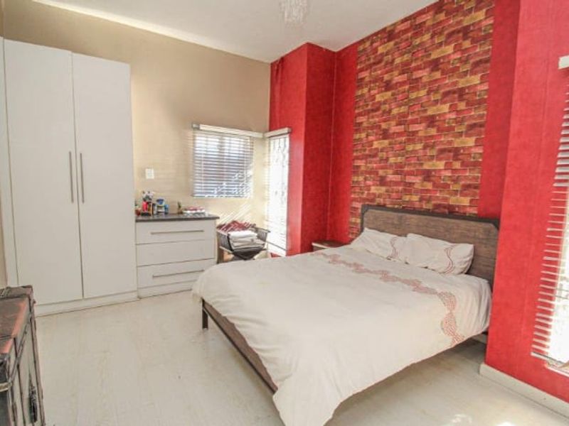 A bedroom featuring a brick-effect accent wall, built-in white wardrobe cabinetry, and venetian blinds on the windows.