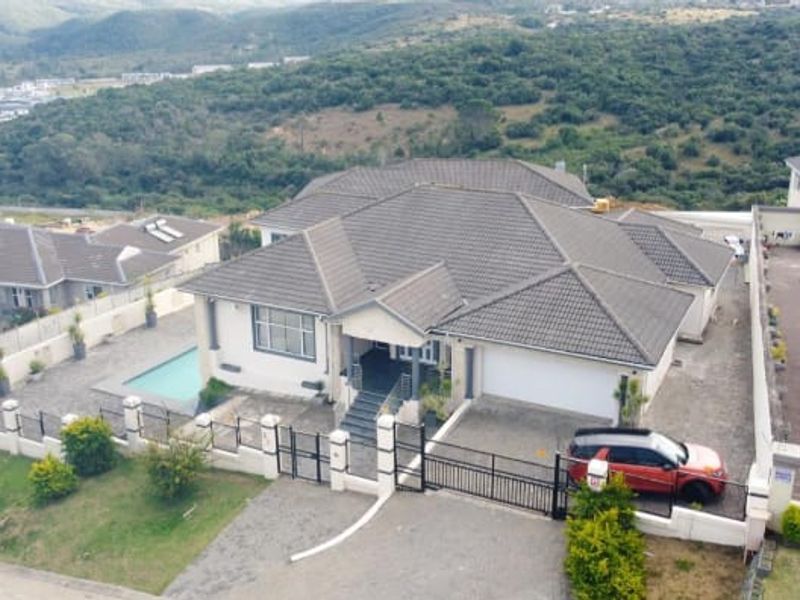 Aerial view of a residential property featuring a tiled roof, swimming pool, paved driveway, and secure perimeter fencing in a hillside estate setting.