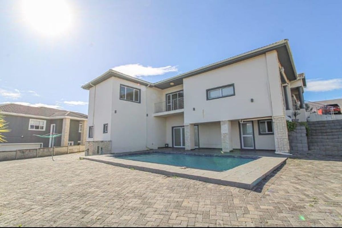 Rear exterior view of the house featuring a swimming pool, paved patio area, and a balcony overlooking the backyard.