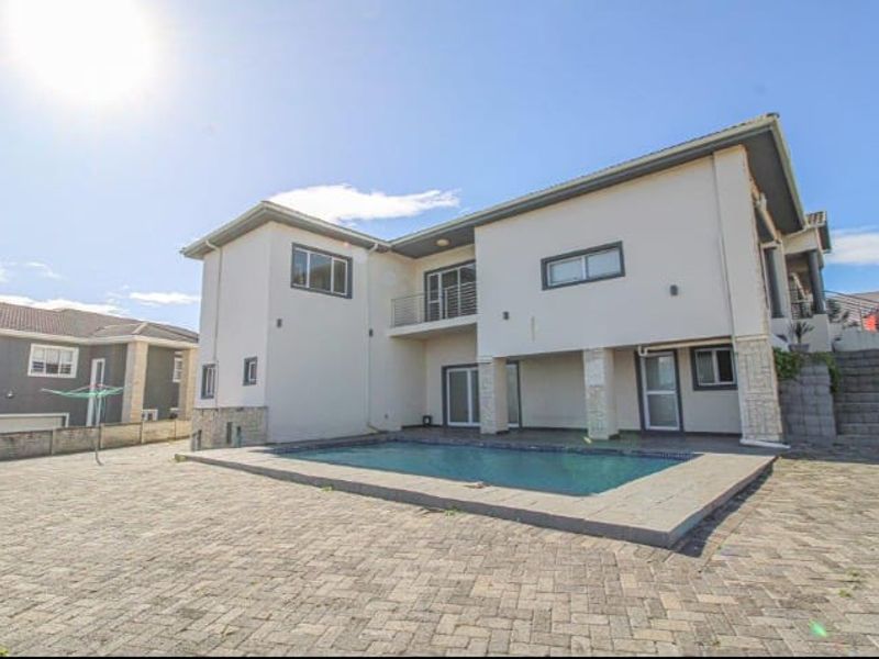 Rear exterior view of the house featuring a swimming pool, paved patio area, and a balcony overlooking the backyard.