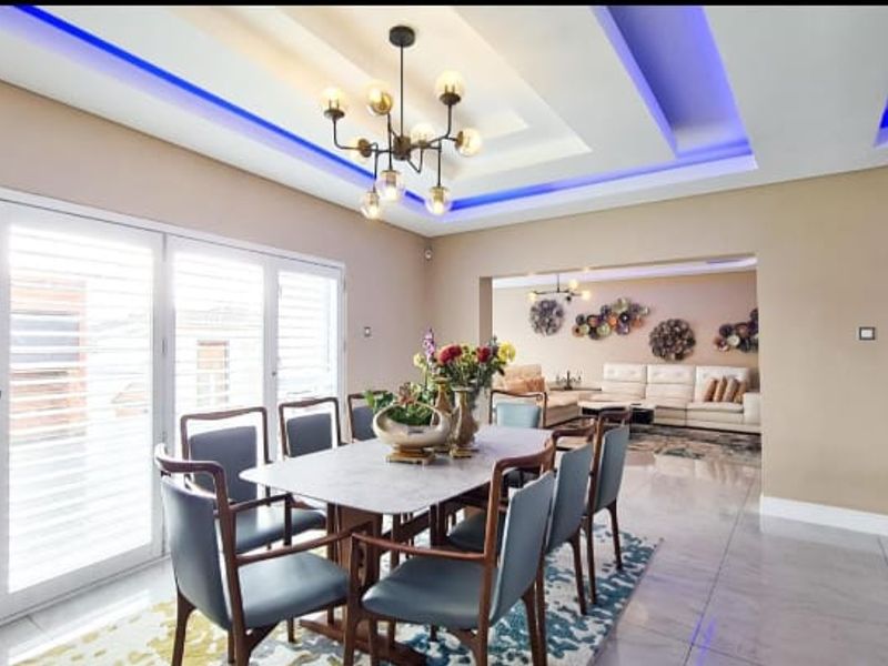 Spacious open-plan dining and living area featuring a modern tray ceiling with integrated LED lighting, tiled floors, and large sliding doors with plantation shutters.