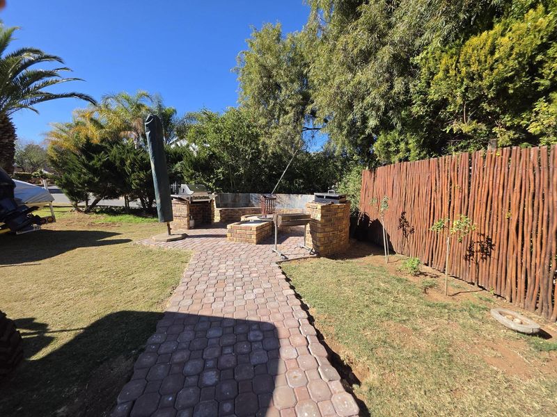 Outdoor entertainment area featuring a brick paved pathway leading to a built-in brick braai and integrated seating, enclosed by a wooden pole fence.