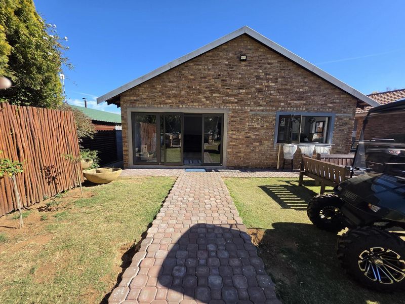 Rear view of a brick-faced house featuring a paved walkway leading to sliding glass doors and a well-maintained garden area.