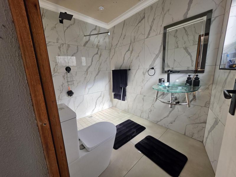 Modern bathroom featuring marble-look wall tiles, a walk-in shower with a rain shower head, and a contemporary wall-mounted glass basin.