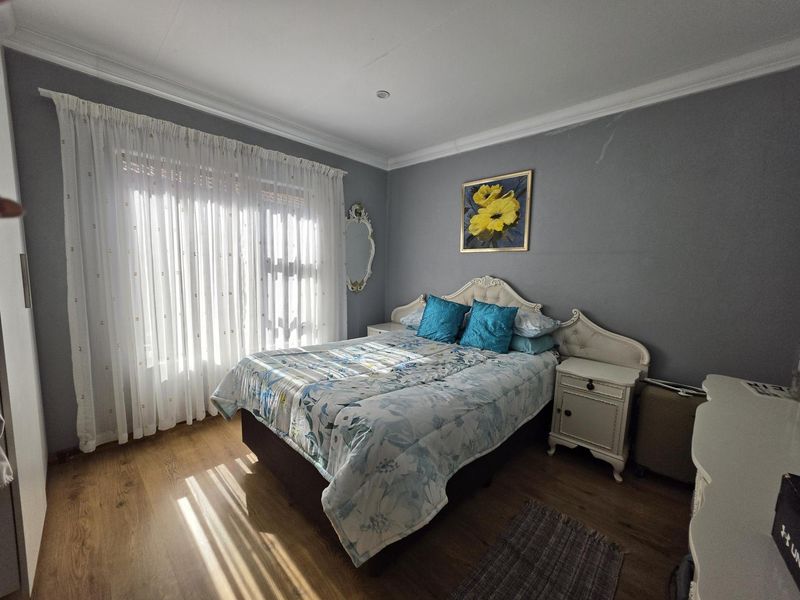 A well-lit bedroom featuring laminate flooring, coved ceilings, and neutral grey walls, offering a comfortable and functional sleeping space.