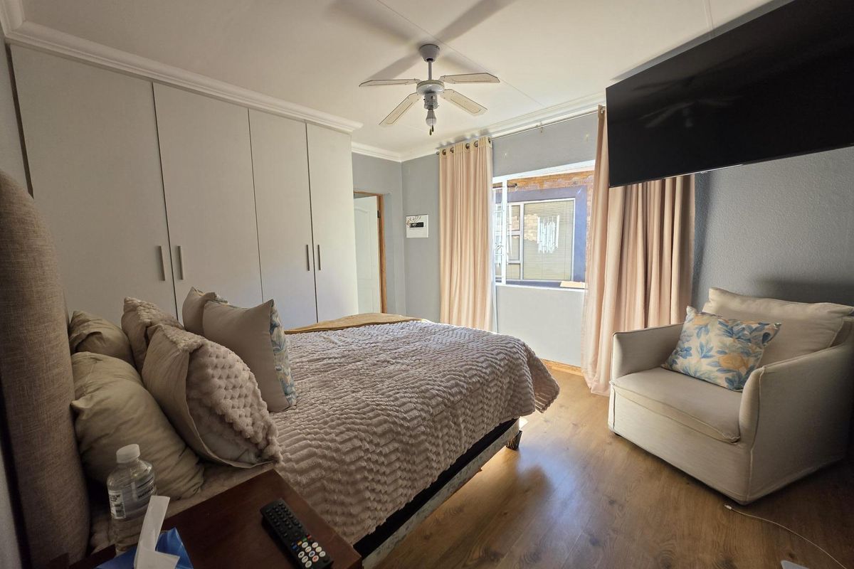A well-maintained bedroom featuring built-in cupboards, laminate flooring, and a ceiling fan, offering a comfortable and functional living space.