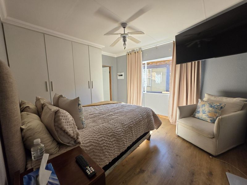 A well-maintained bedroom featuring built-in cupboards, laminate flooring, and a ceiling fan, offering a comfortable and functional living space.