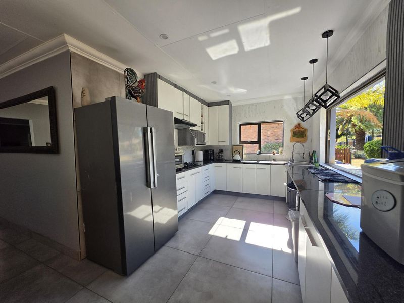 Modern kitchen featuring white cabinetry, dark granite countertops, integrated appliances, tiled flooring, and large windows providing ample natural light.