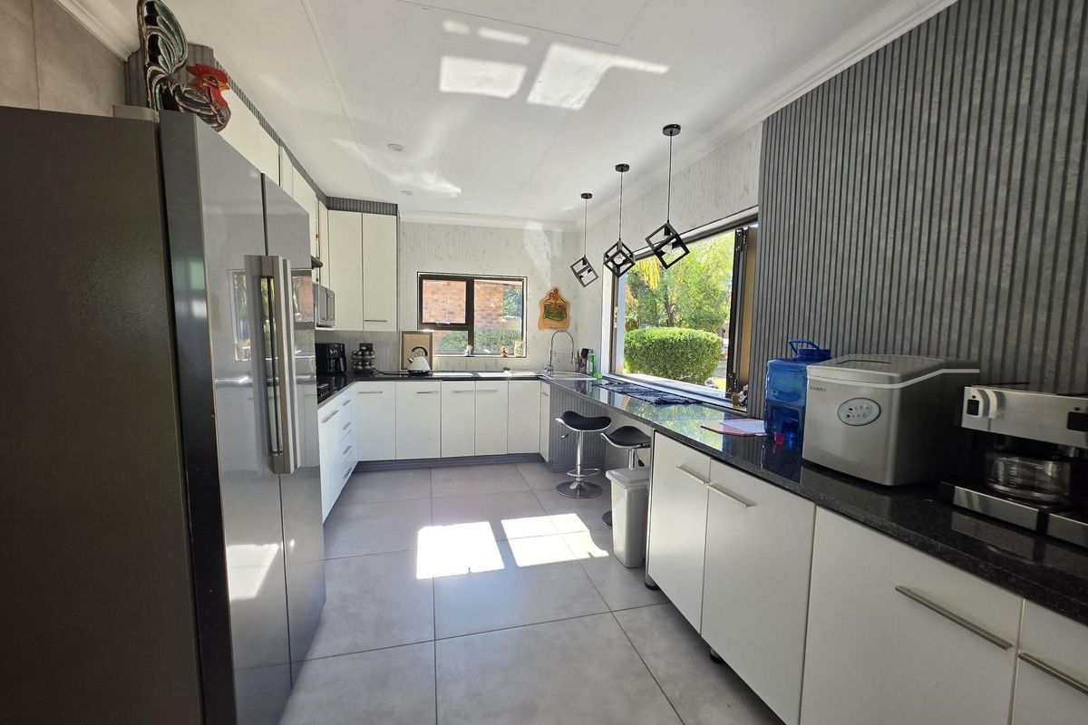 Modern kitchen featuring white cabinetry, dark granite countertops, tiled flooring, and a breakfast bar with pendant lighting overlooking the garden.