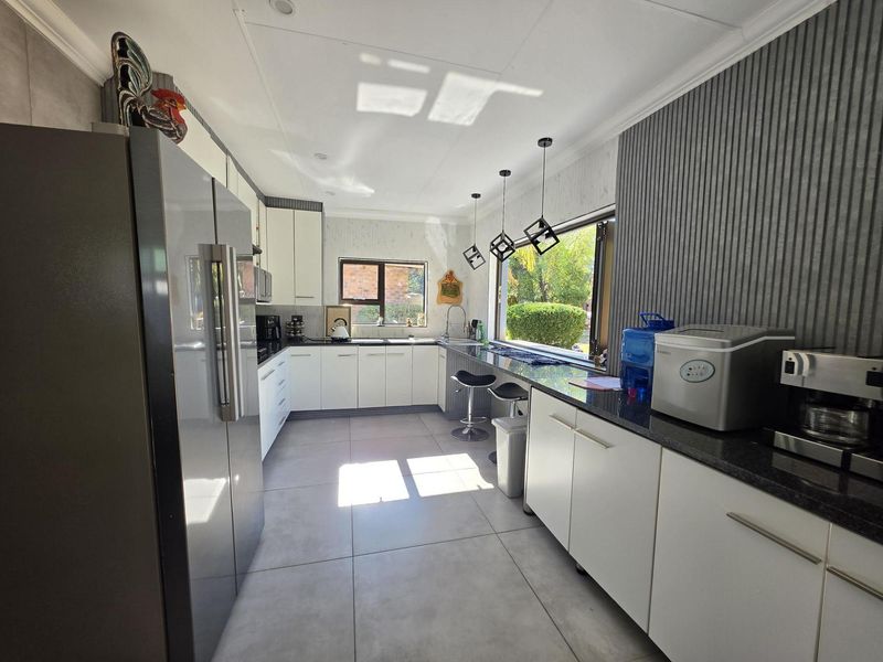 Modern kitchen featuring white cabinetry, dark granite countertops, tiled flooring, and a breakfast bar with pendant lighting overlooking the garden.