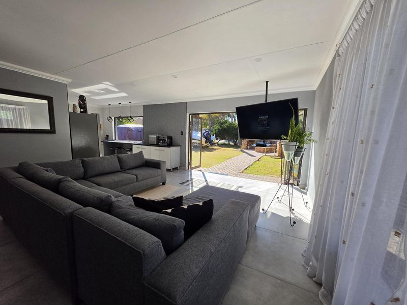 Spacious open-plan living area featuring tiled floors, modern kitchen cabinetry, and seamless indoor-outdoor flow through double glass doors to the garden.