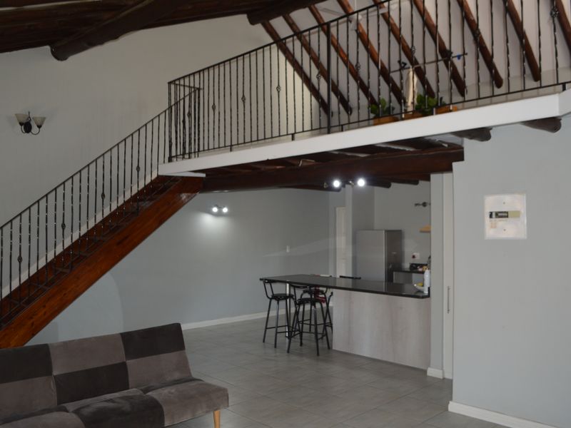 Spacious open-plan living area featuring a mezzanine level, exposed timber beams, a modern kitchen island, and a wrought iron staircase.
