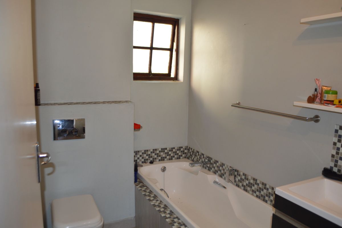 A functional bathroom featuring a built-in bathtub with mosaic tile detailing, a wall-mounted flush system, and a vanity basin.