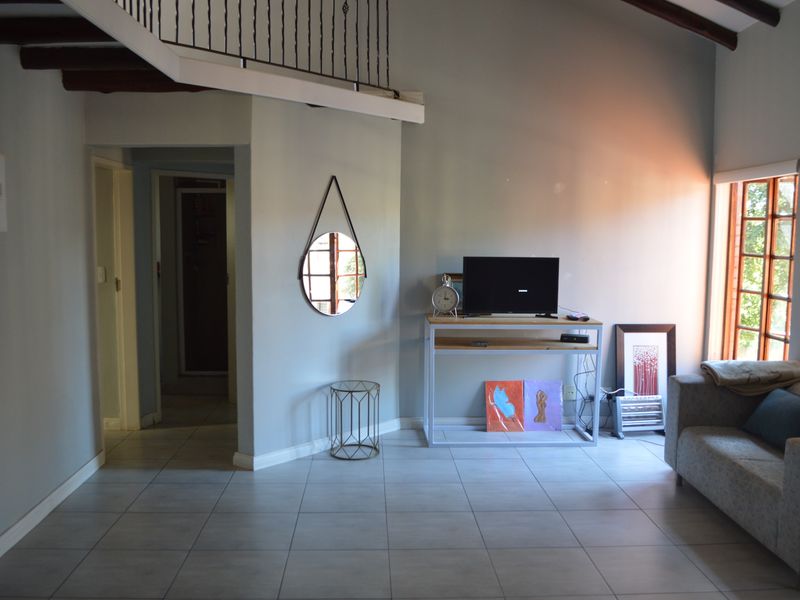 A living room featuring tiled flooring, exposed timber ceiling beams, and a mezzanine level overlooking the space with a timber frame window.