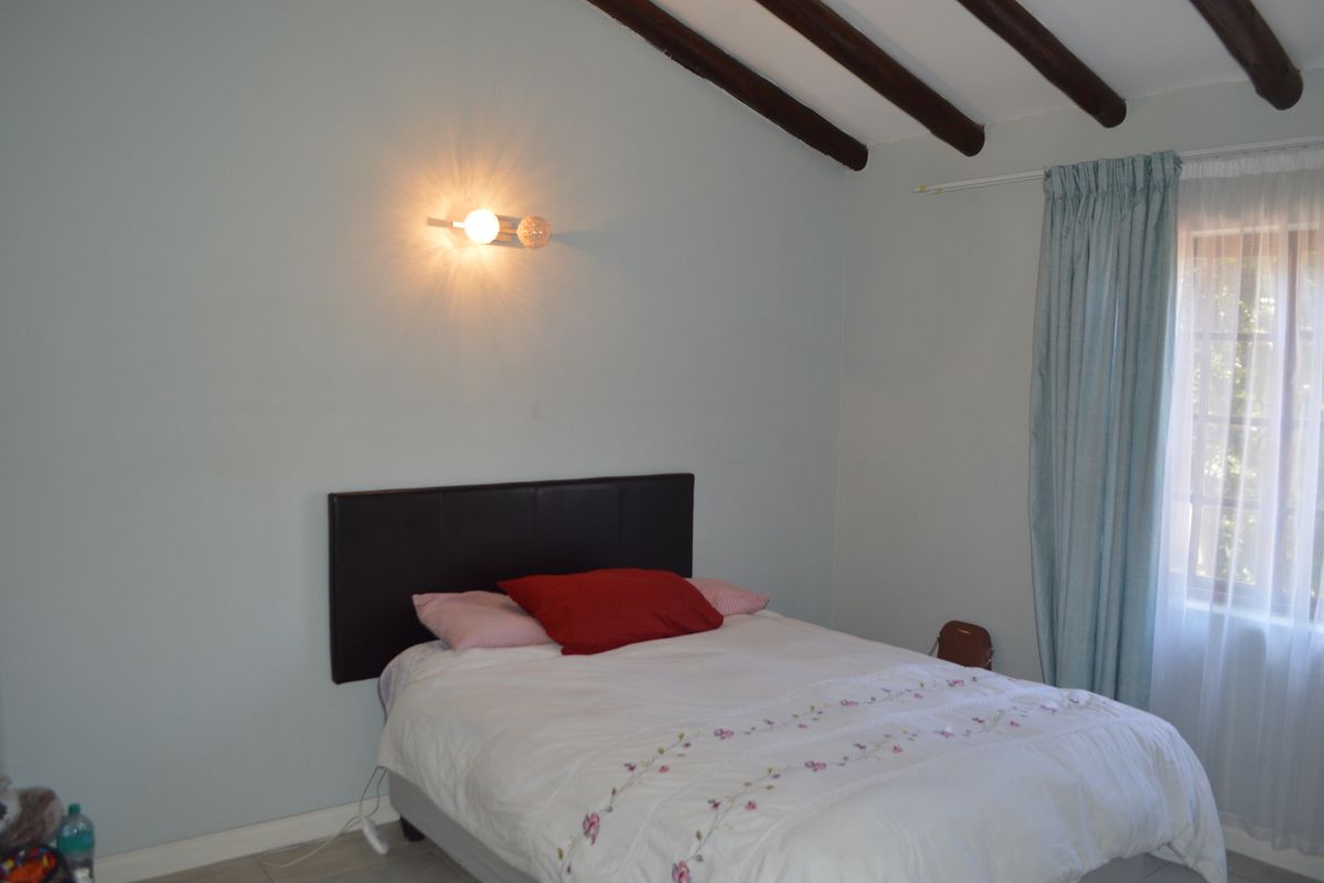 A bedroom featuring exposed timber ceiling beams, a wall-mounted light fixture, and a window with curtain rails.