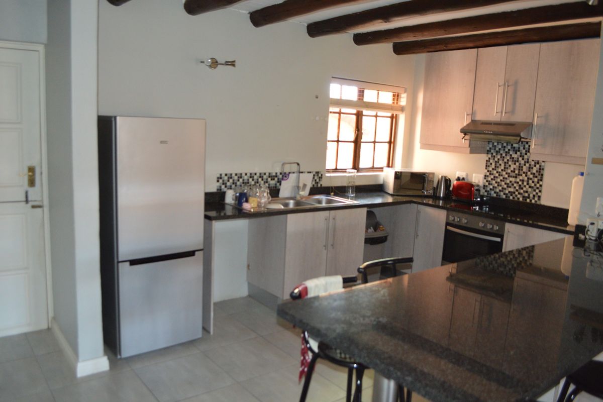A functional kitchen featuring granite countertops, a mosaic backsplash, built-in oven with extractor, and rustic exposed timber ceiling beams.