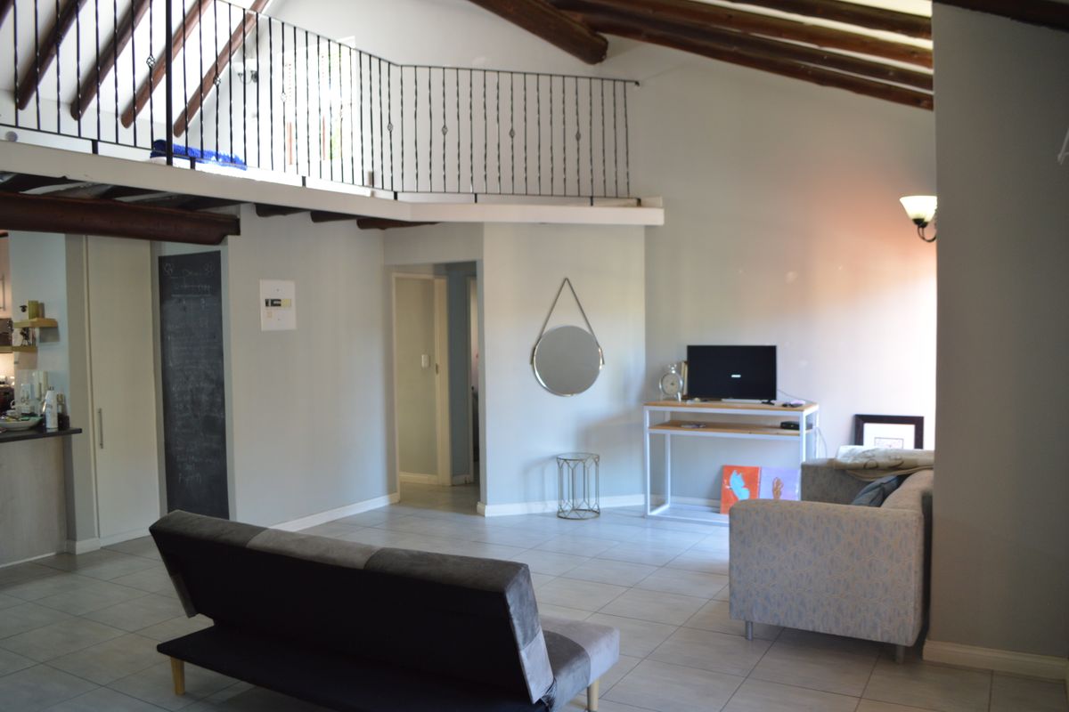 Spacious living area featuring a mezzanine level with wrought iron balustrade, exposed timber ceiling beams, and neutral tiled flooring.
