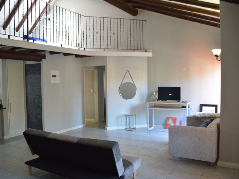 Spacious living area featuring a mezzanine level with wrought iron balustrade, exposed timber ceiling beams, and neutral tiled flooring.