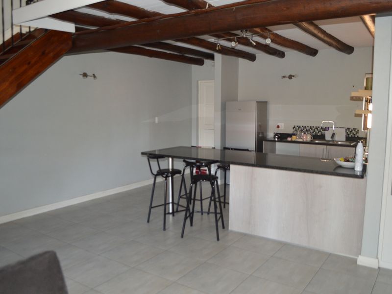 Open plan living area featuring a kitchen with granite countertops, tiled flooring, and exposed timber ceiling beams, with an integrated staircase.