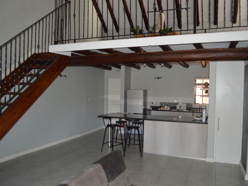 Open-plan living area featuring a modern kitchen with island, tiled flooring, and a striking mezzanine level accessed by a wrought iron staircase.
