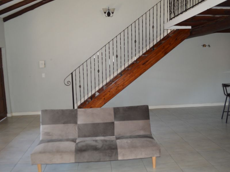 Spacious living area featuring exposed timber ceiling beams, a timber staircase with a decorative wrought iron balustrade, and neutral tiled flooring.