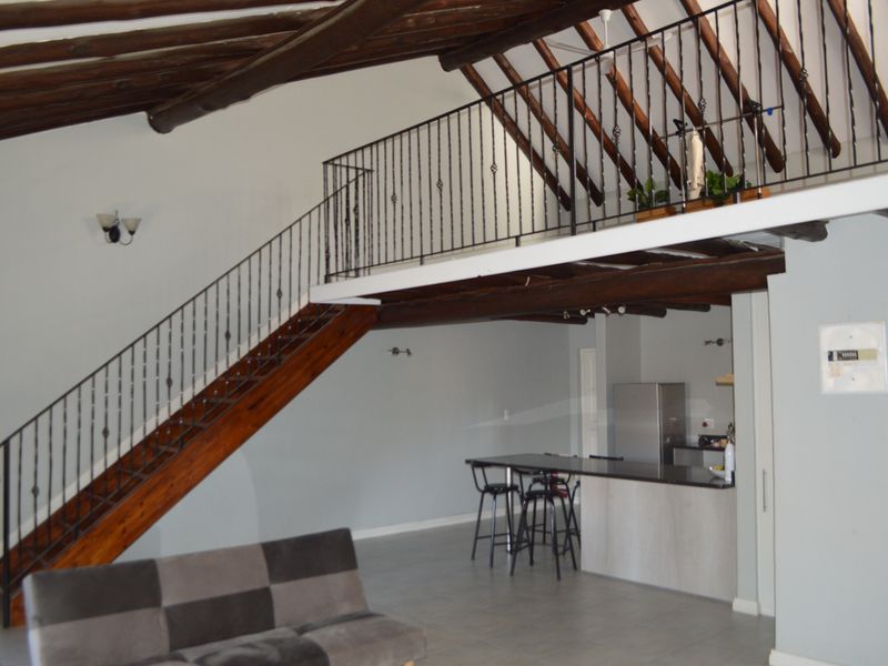 Spacious open-plan living area featuring a mezzanine level, exposed timber beams, a wrought iron staircase, and a functional kitchen island.