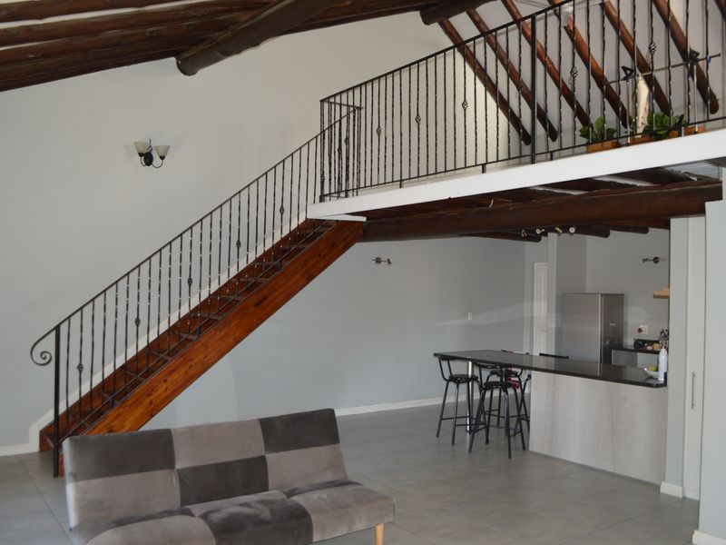 Open plan living area featuring a mezzanine level, exposed timber beams, a kitchen island, and a wrought iron staircase.