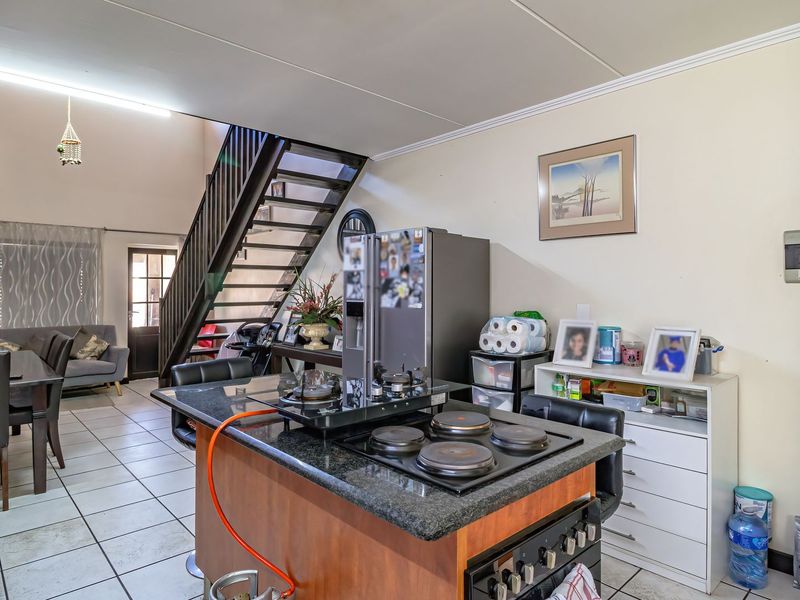Open-plan living area featuring a kitchen island with a built-in hob, tiled flooring, and a staircase leading to the upper level.