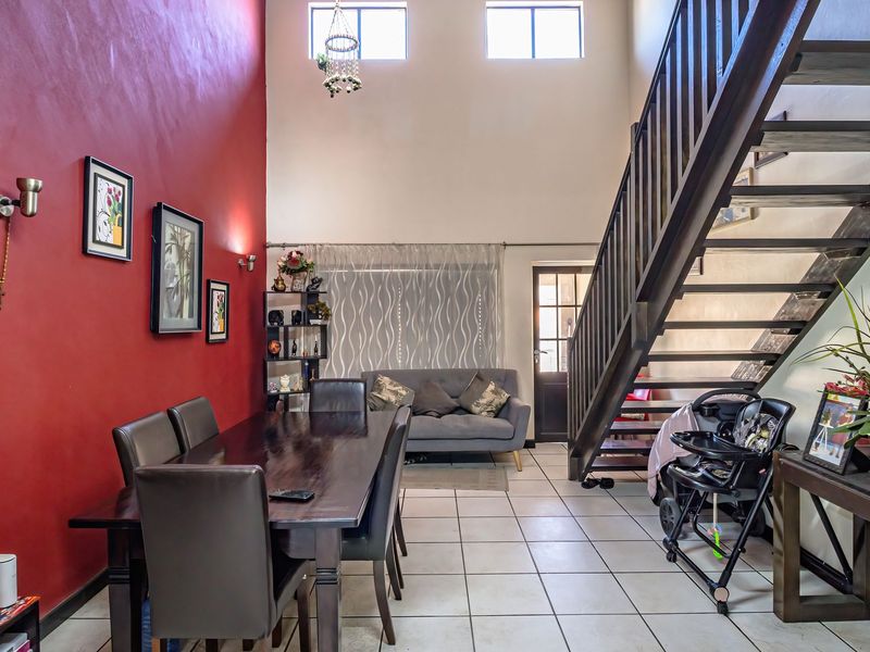 Spacious open-plan living and dining area featuring high ceilings, tiled flooring, and a prominent staircase leading to the upper level.