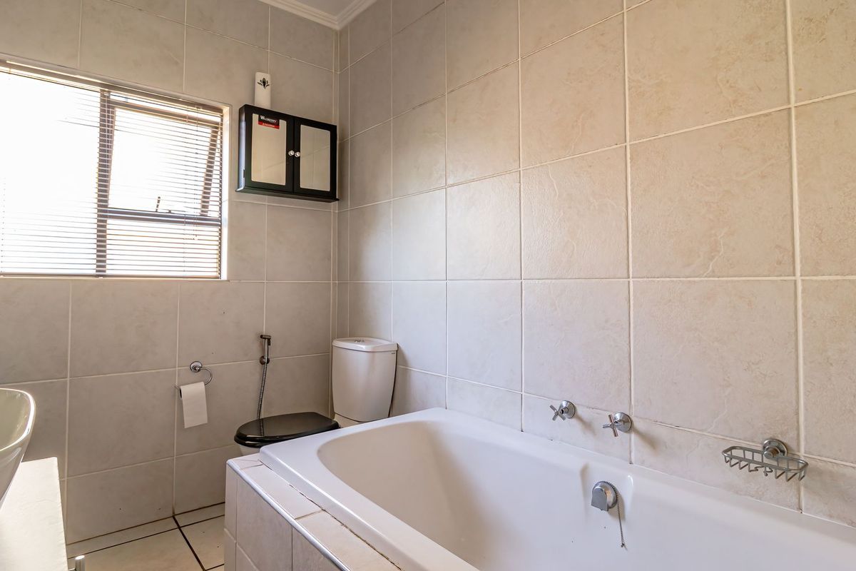 A functional bathroom featuring a built-in bathtub, toilet, and wall-mounted storage cabinet, finished with neutral wall and floor tiling.