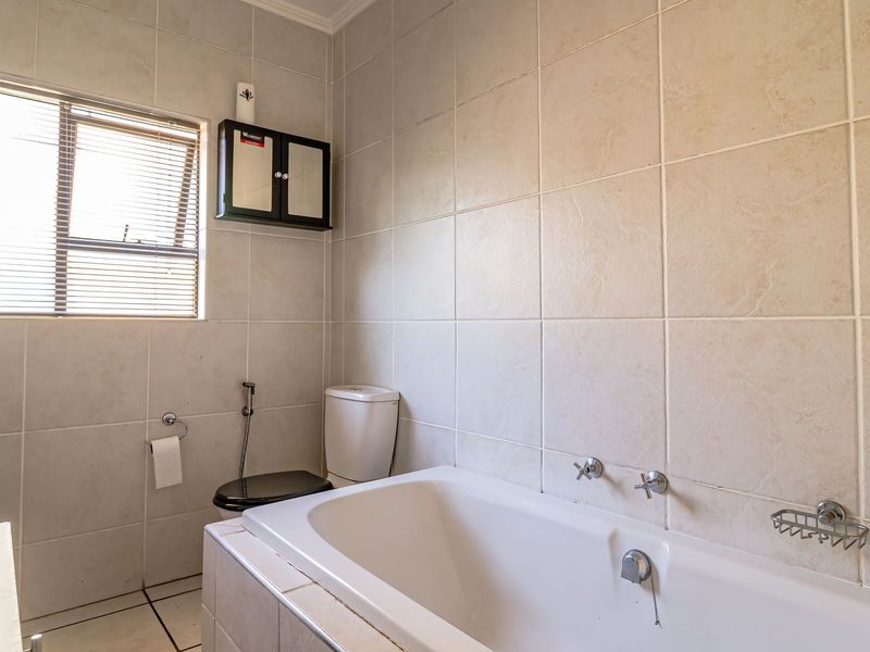 A functional bathroom featuring a built-in bathtub, toilet, and wall-mounted storage cabinet, finished with neutral wall and floor tiling.