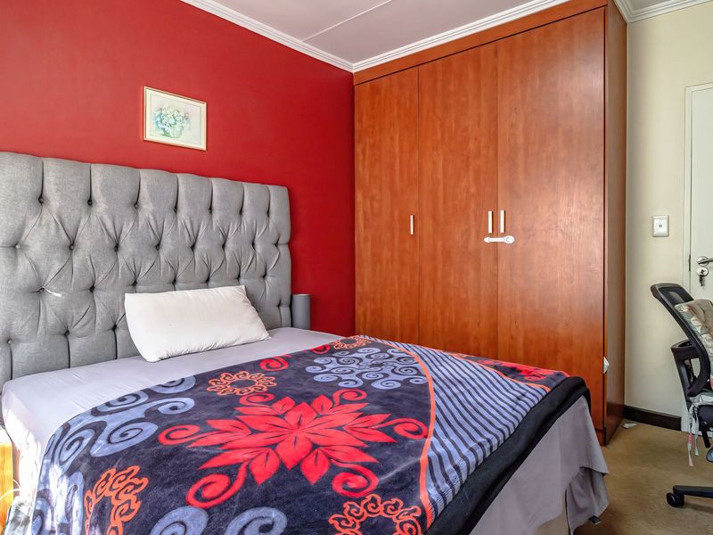 A bedroom featuring a built-in wooden wardrobe, coving, and a bold red accent wall.